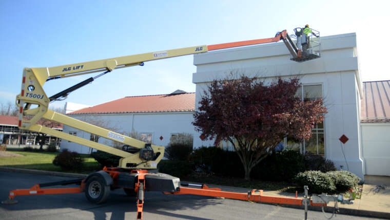 Bear Rental employee putting up Christmas lights with a tow-behind lift